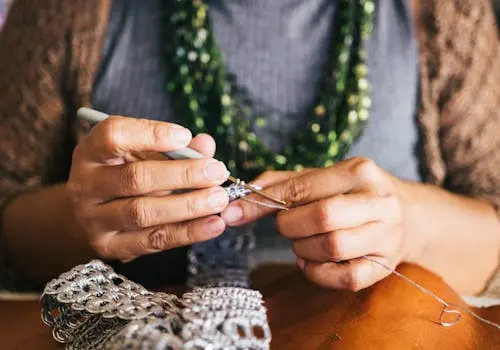 mulher com agulha e linha branca tecendo crochê